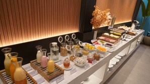 Un bufé con diversos alimentos y bebidas, incluyendo frascos de miel, cestas de fruta y una selección de quesos.