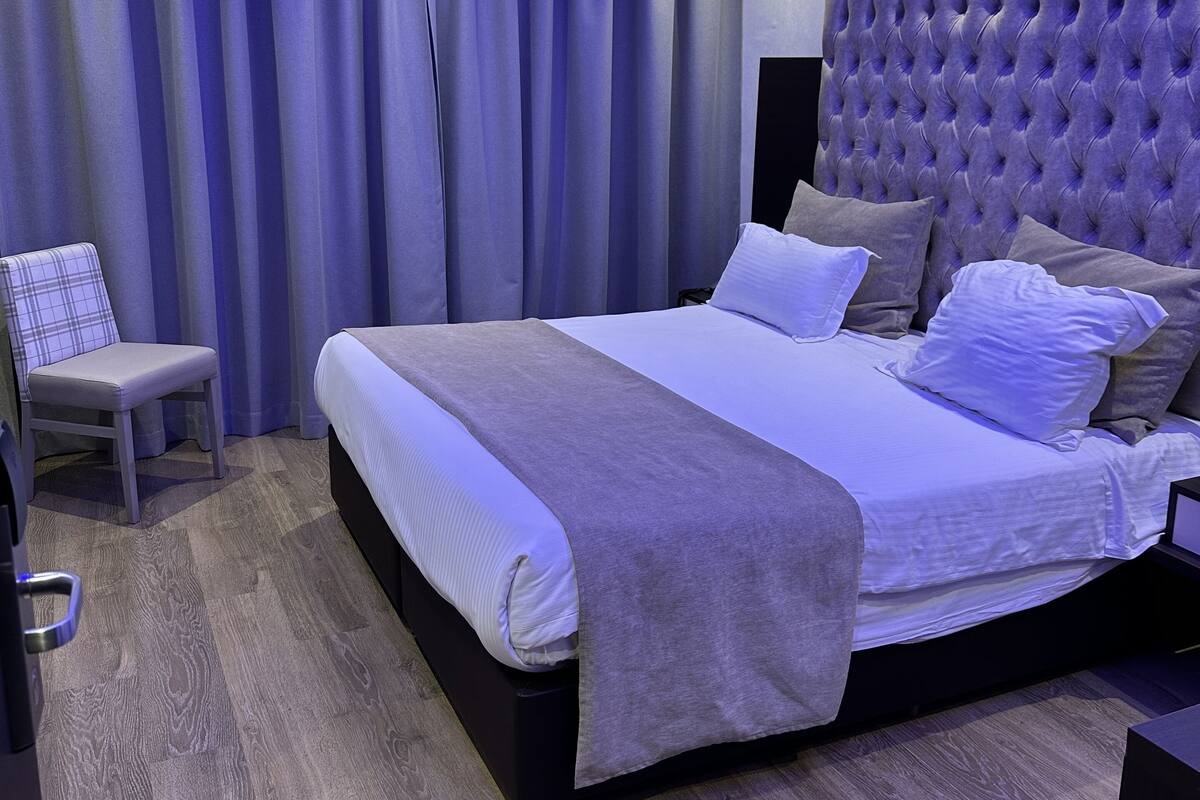 A modern bedroom with a large bed, a chair, and a ceiling with blue lighting.