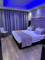 A modern bedroom with a large bed, a chair, and a ceiling with blue lighting.