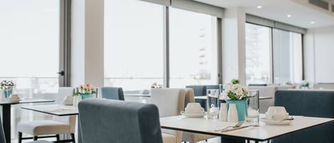 Un comedor moderno con mesas dispuestas para dos, con un diseño minimalista, sillas tapizadas en gris y vajilla blanca.
