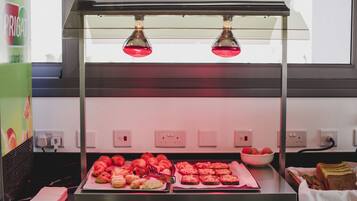 A food display with pastries and bread under a glass enclosure with two lights.