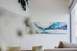 A modern living room with a large abstract painting on the wall, a sofa with cushions, and a window providing natural light.