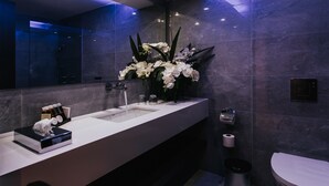 A modern bathroom with a white sink, a mirror, and a vase of white flowers.