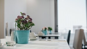 A dining table with a blue pot of flowers, a glass of water, and a white cup.