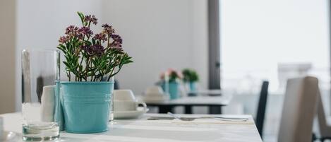A dining table with a blue pot of flowers, a glass of water, and a white cup.