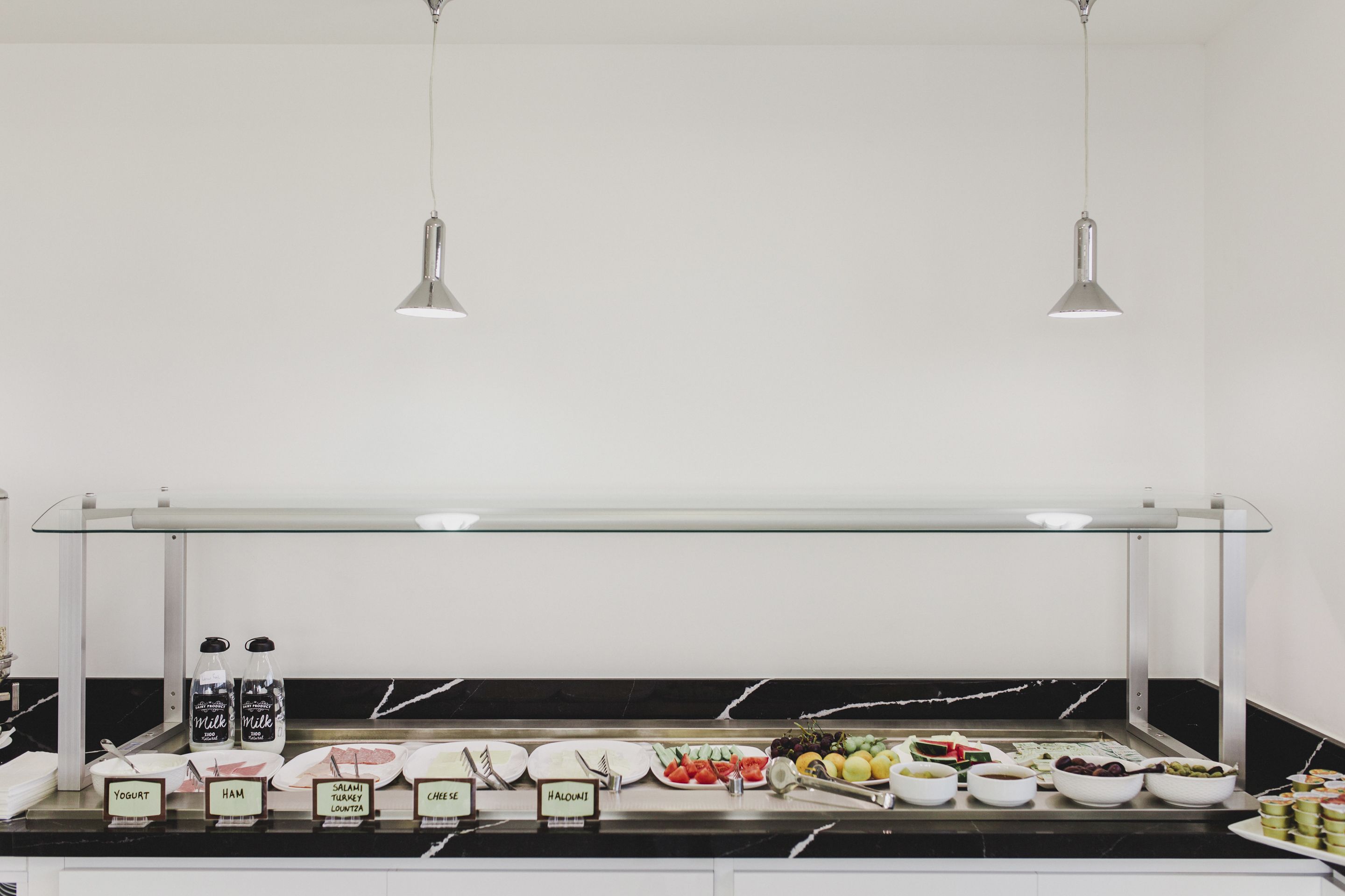 Un buffet proposant une variété d'aliments, chacun étant clairement identifié, notamment du yaourt, du jambon, du salami, du fromage et du halloumi.