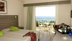 Une chambre d’hôtel avec un lit, une petite table avec des chaises, un balcon donnant sur l’océan et une machine à café sur la table.
