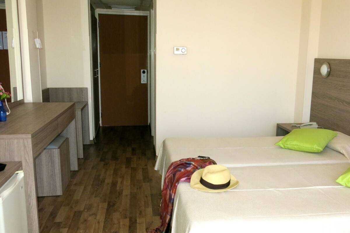 A hotel room with two beds, a desk, a chair, and a door leading to a hallway.