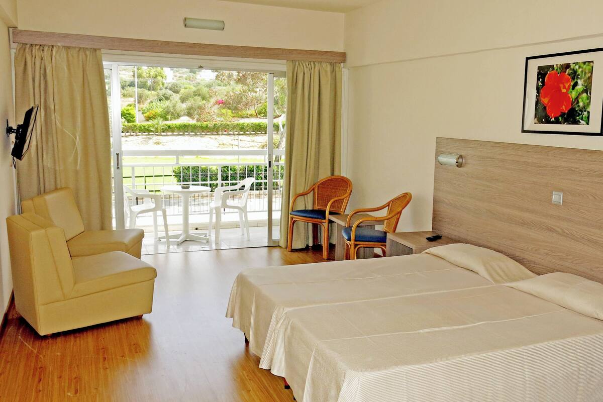 Habitación de hotel con dos camas, una silla, una mesa y un balcón con sillas.