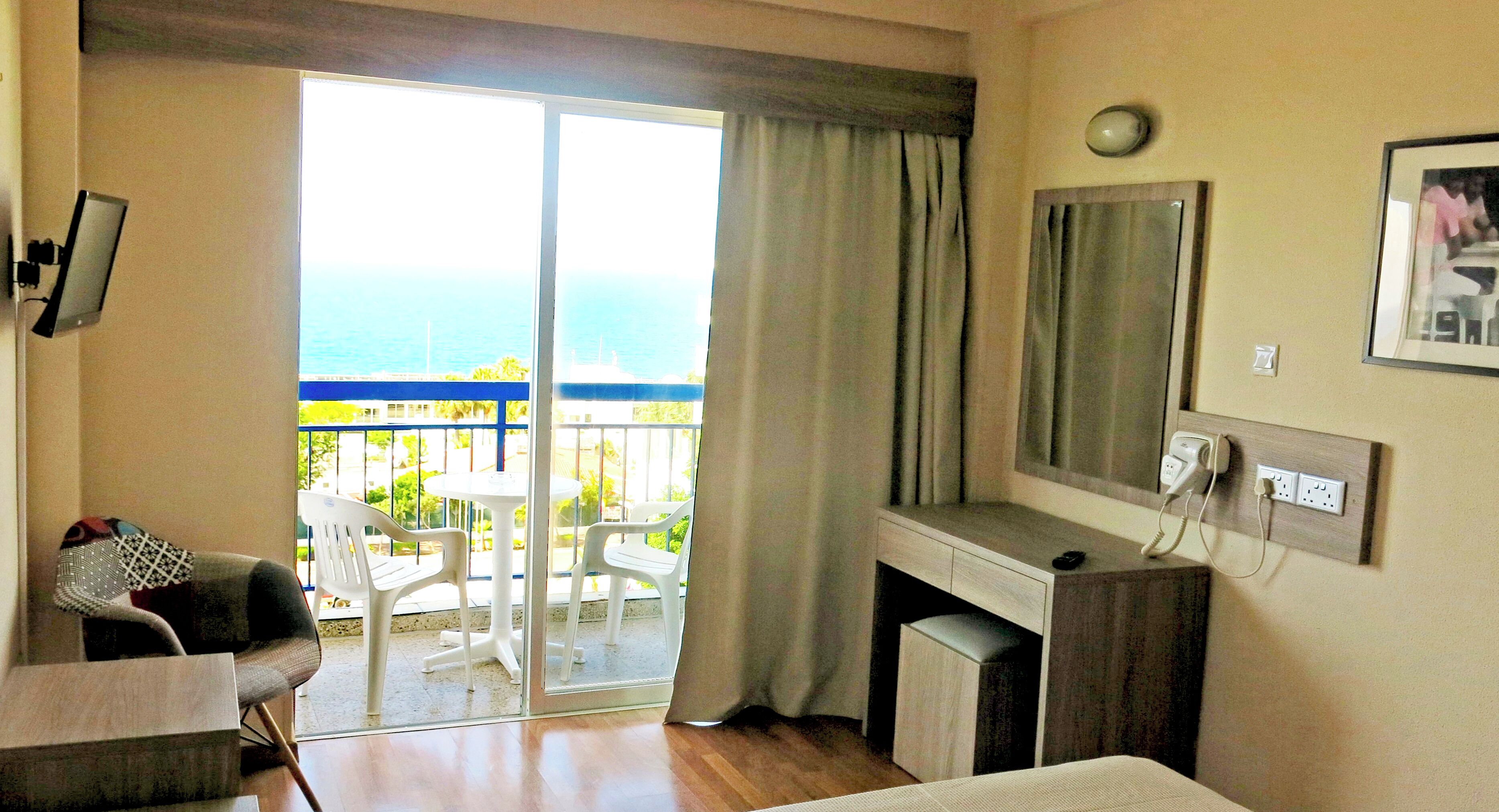 Une chambre d’hôtel avec un balcon, un bureau, une chaise, un lit, une télévision et un miroir.