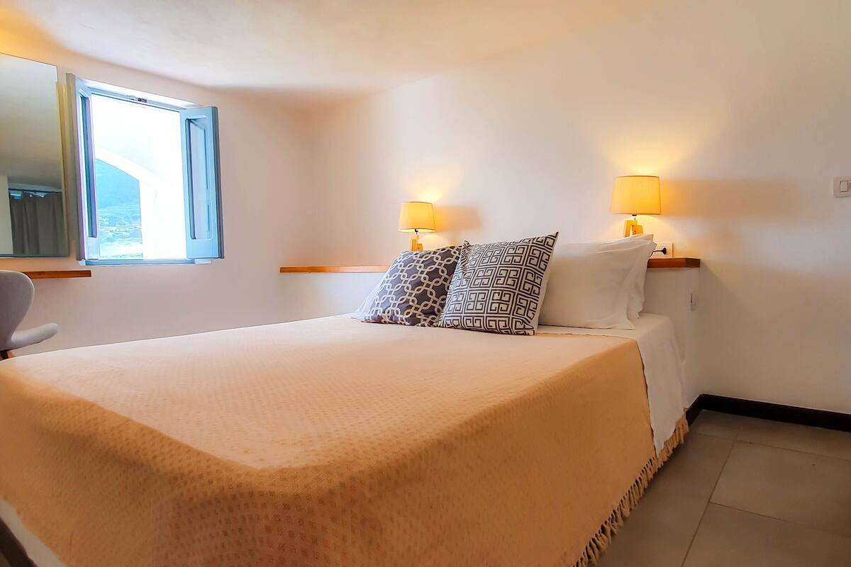 Een hotelkamer met een bed, twee bedlampen, een stoel, een raam en een spiegel.