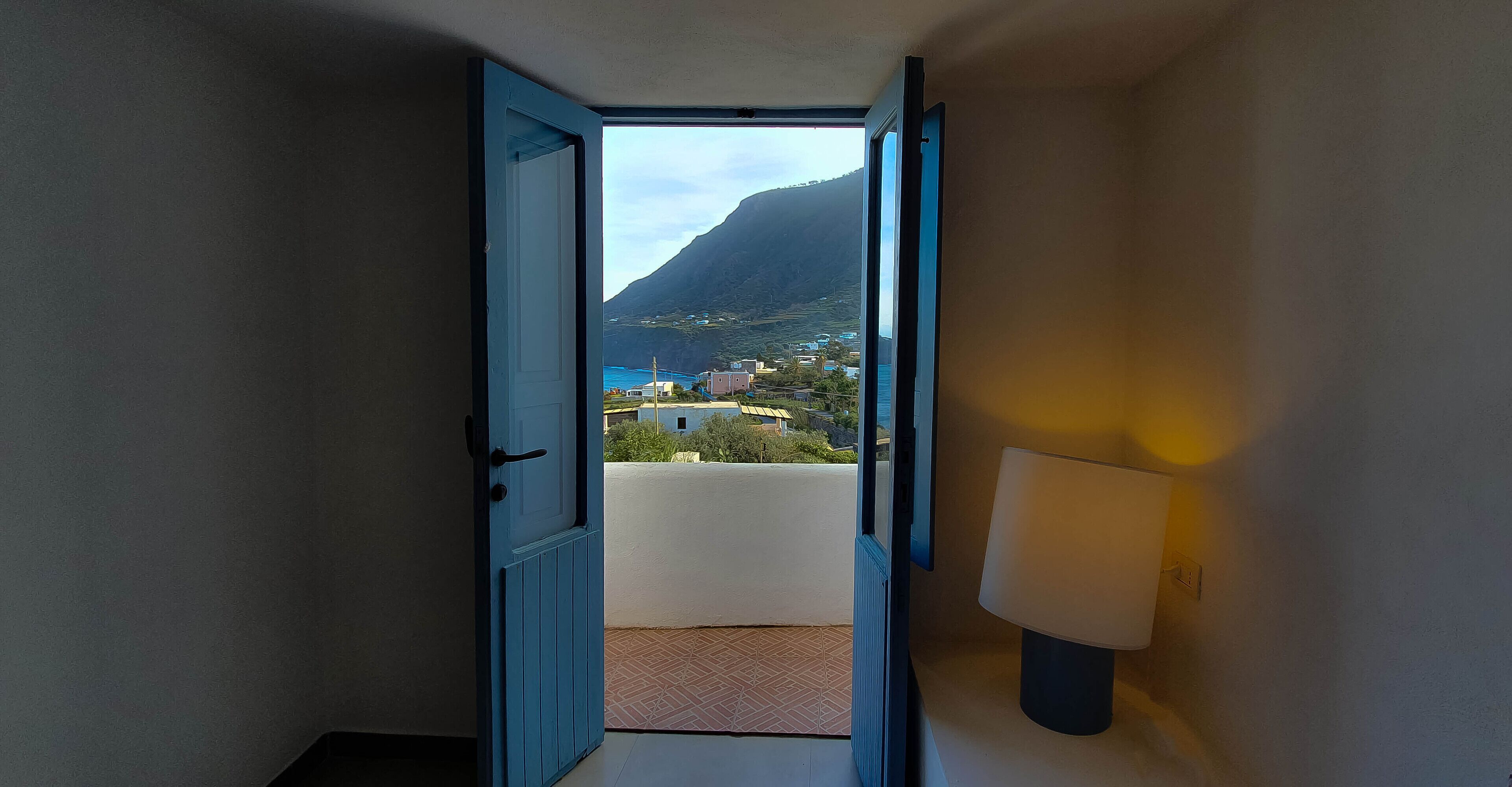 Ein Flur mit einer blauen Tür, der zu einem Balkon mit Blick auf einen Berg und Gebäude führt.