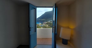 Un couloir avec une porte bleue qui donne sur un balcon offrant une vue sur une montagne et des bâtiments.