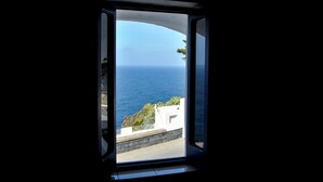 Una ventana con vista al mar y un edificio blanco con muro de piedra.
