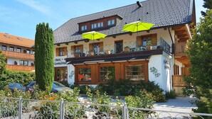 Un hotel de estilo arquitectónico europeo tradicional, con un balcón con plantas en macetas, un jardín bien cuidado y un cielo despejado.
