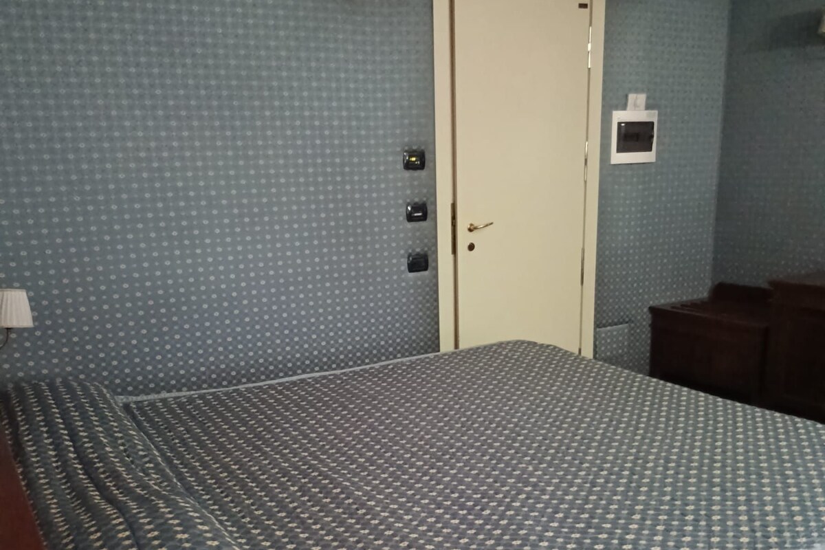 A bedroom with a bed, a nightstand, a lamp, and a door.