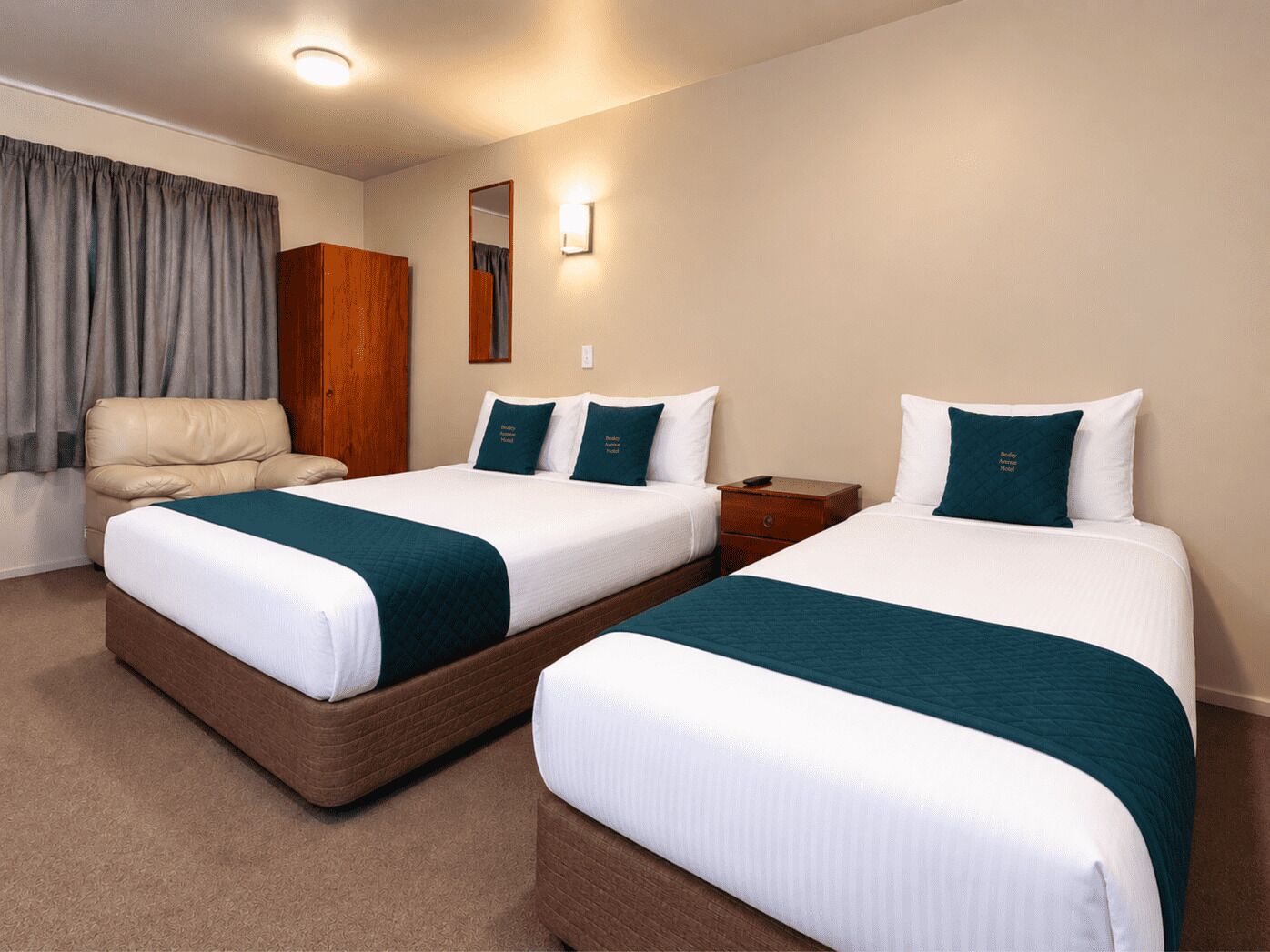 A hotel room with two beds, a sofa, a wooden wardrobe, and a mirror.