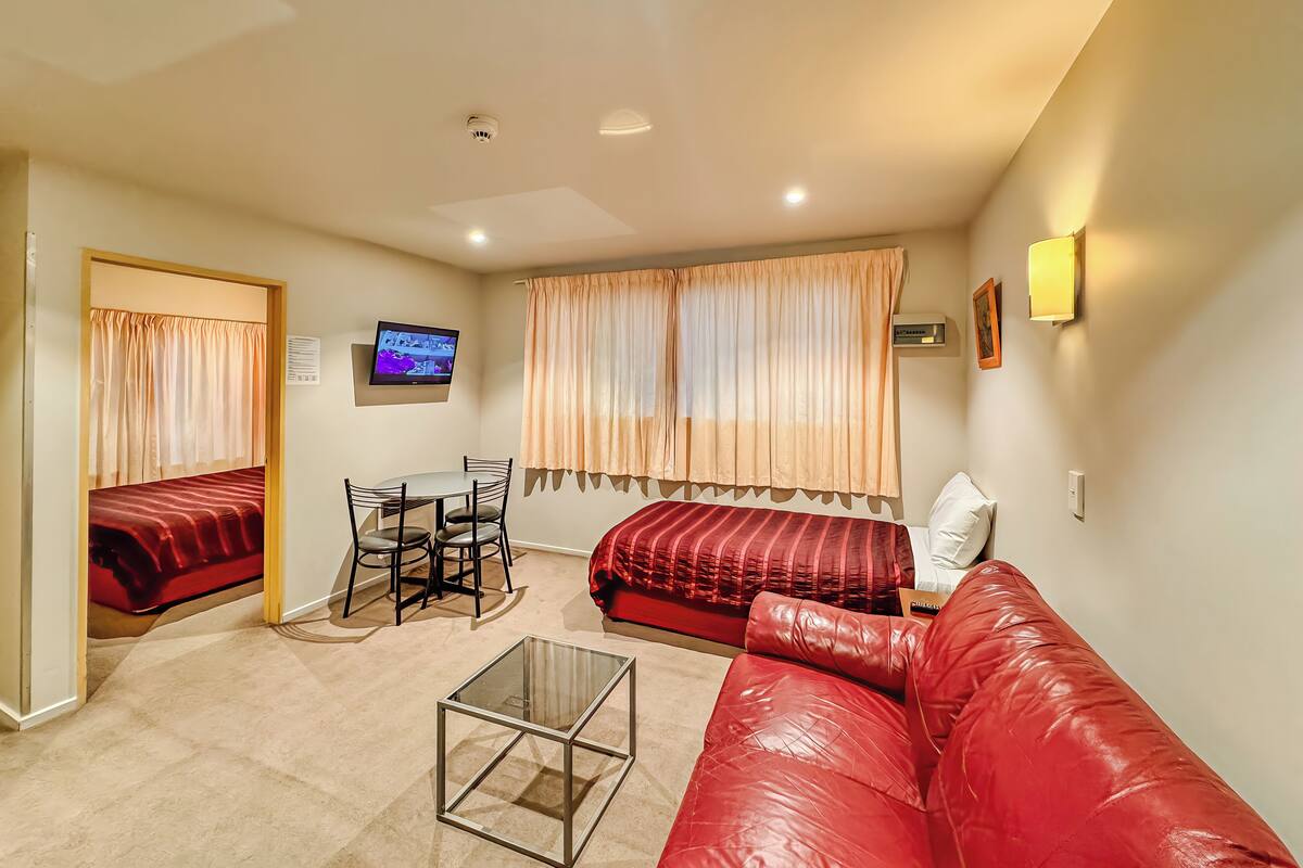 A compact hotel room with a bed, a sofa, a small table, a TV, and a window with curtains.