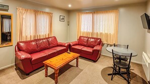 Una sala de estar con dos sofás de cuero rojo, una mesa de centro de madera, una mesa de comedor con sillas y un televisor de pantalla plana montado en la pared.