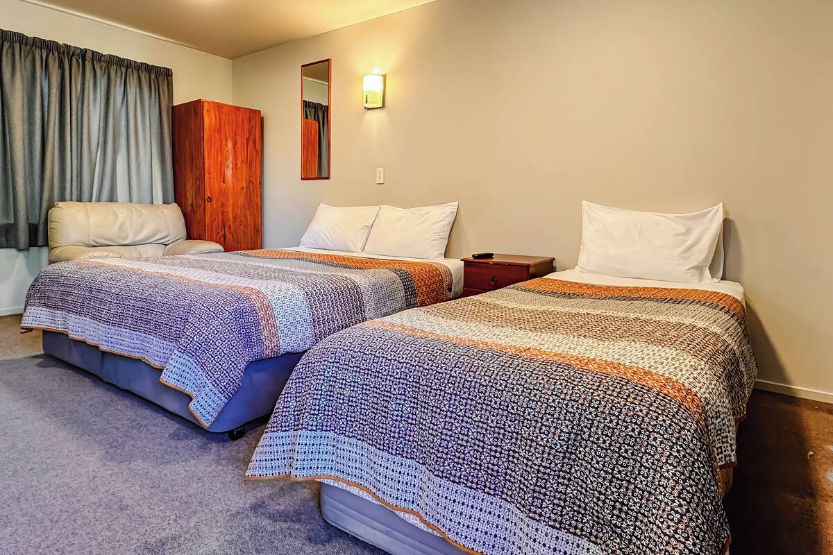 A hotel room with two beds, a wooden wardrobe, a mirror, and a light fixture.