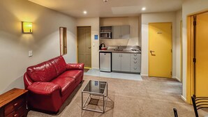 Un espacio habitable compacto con un sofá de cuero rojo, una mesa de centro de vidrio, una kitchenette y una puerta amarilla.