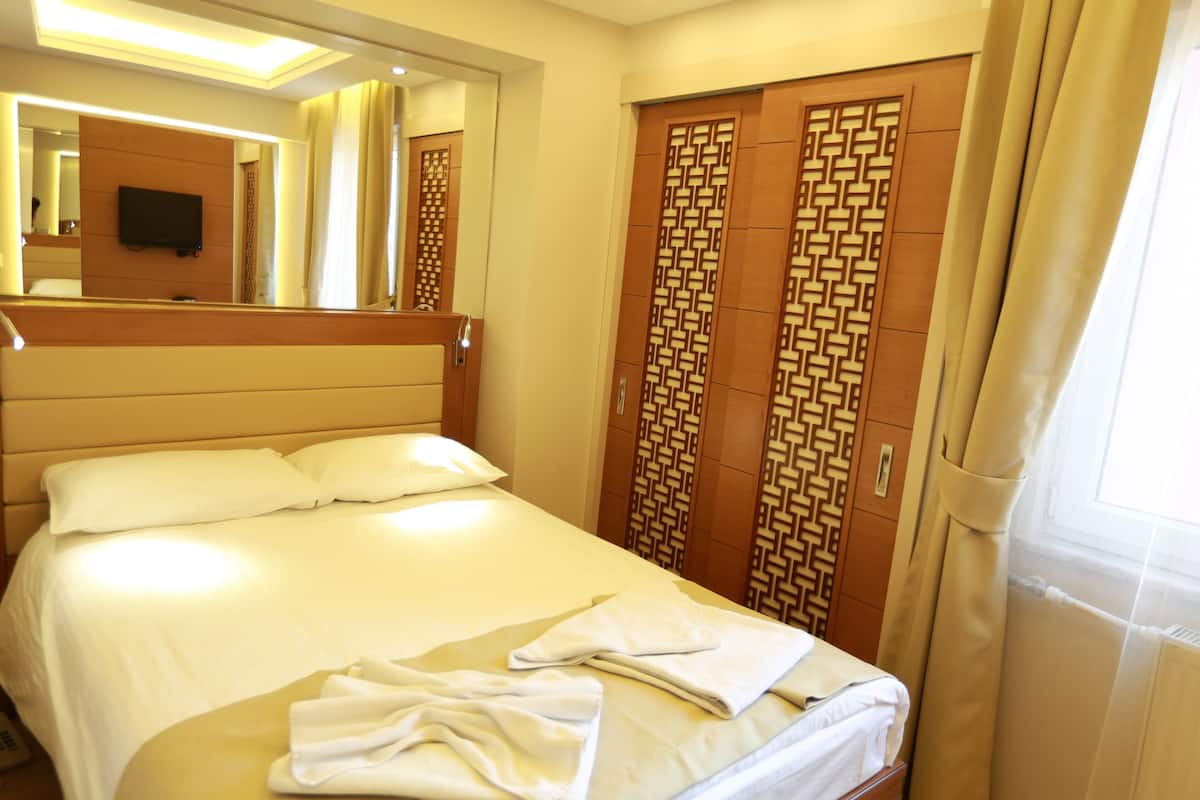 A hotel room with a large bed, a mirror, a television, and a wardrobe with a geometric pattern.