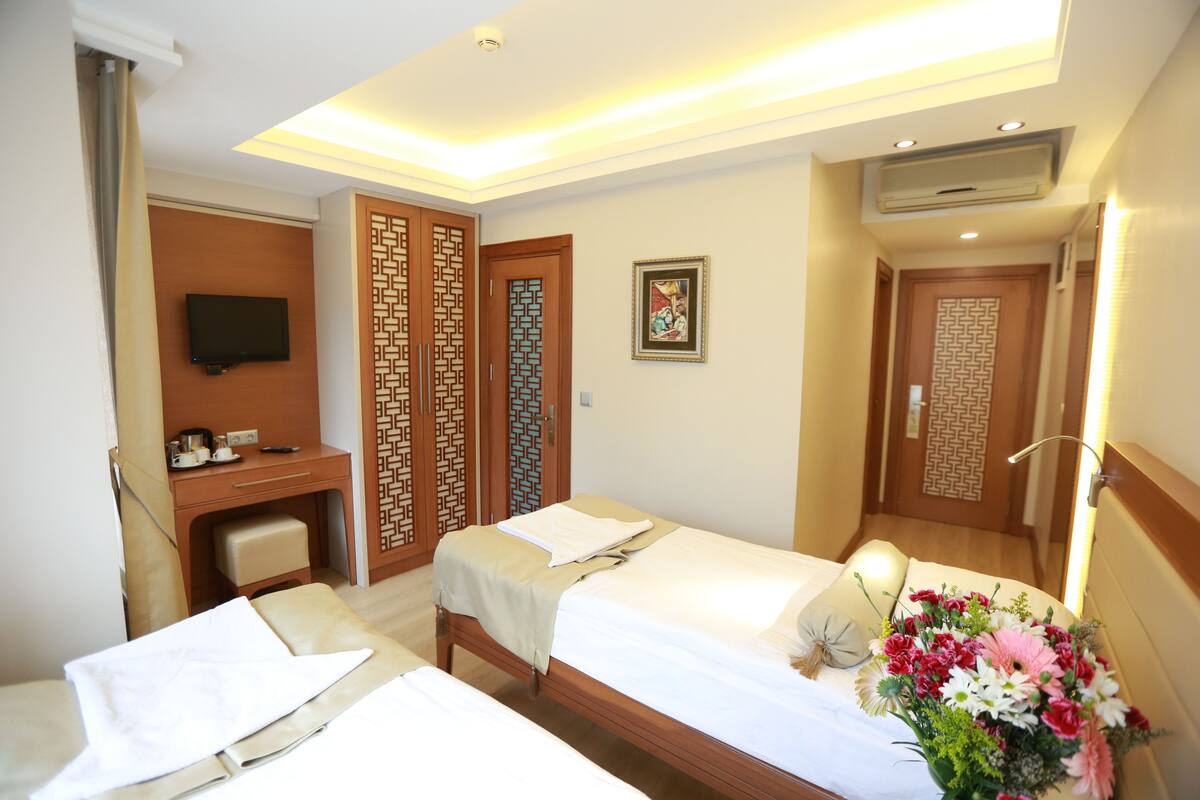 A hotel room with two beds, a desk, a television, and a decorative wall panel.