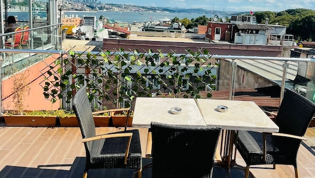 Une terrasse sur le toit, avec une table et des chaises, d’où l’on peut admirer un panorama urbain avec ses bâtiments et une étendue d’eau.