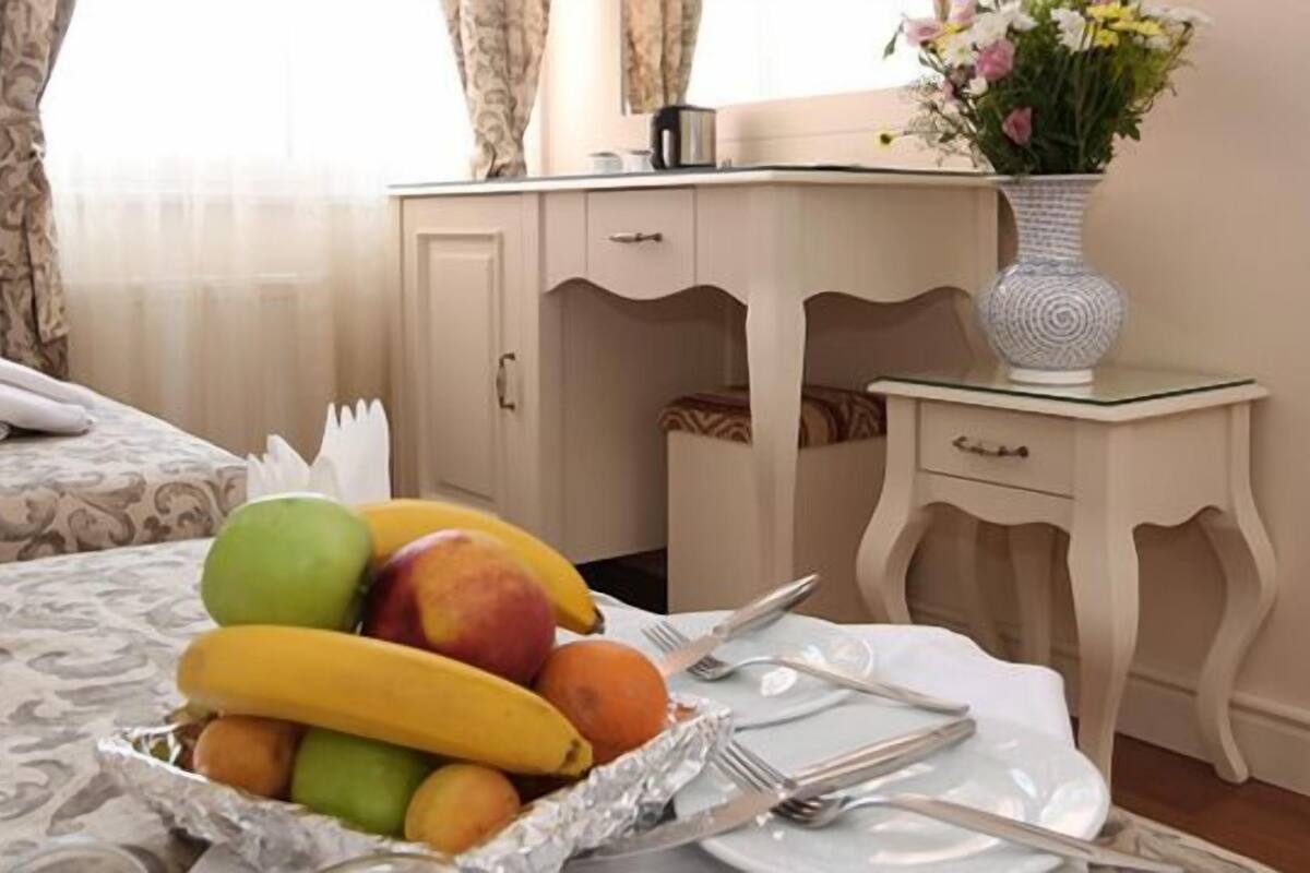 A neatly made bed with a patterned bedspread, a bedside table with a vase of flowers, and a fruit bowl on the nightstand.