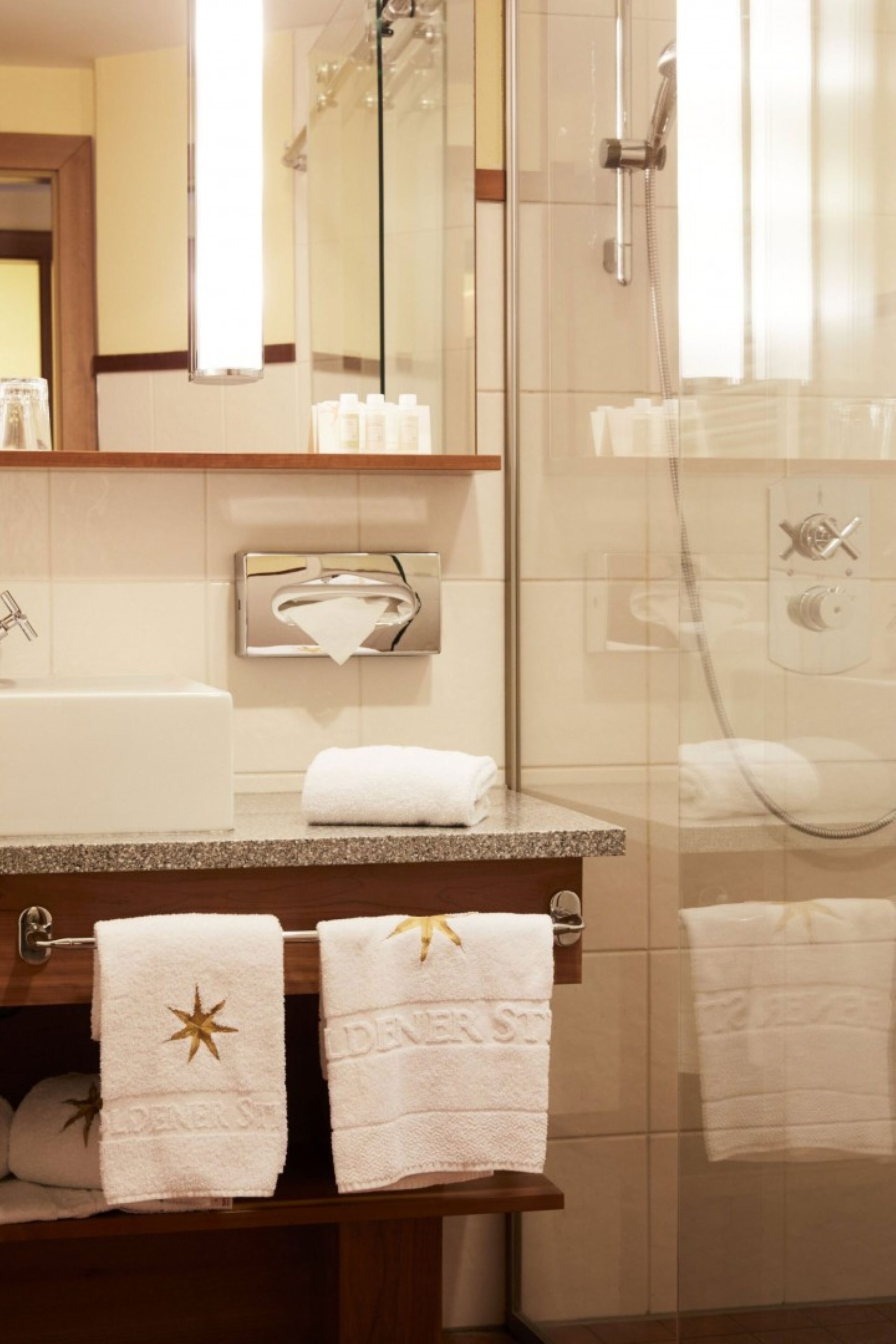 A modern bathroom with a glass-enclosed shower, a sink with a mirror above it, and two towels with star and text designs.
