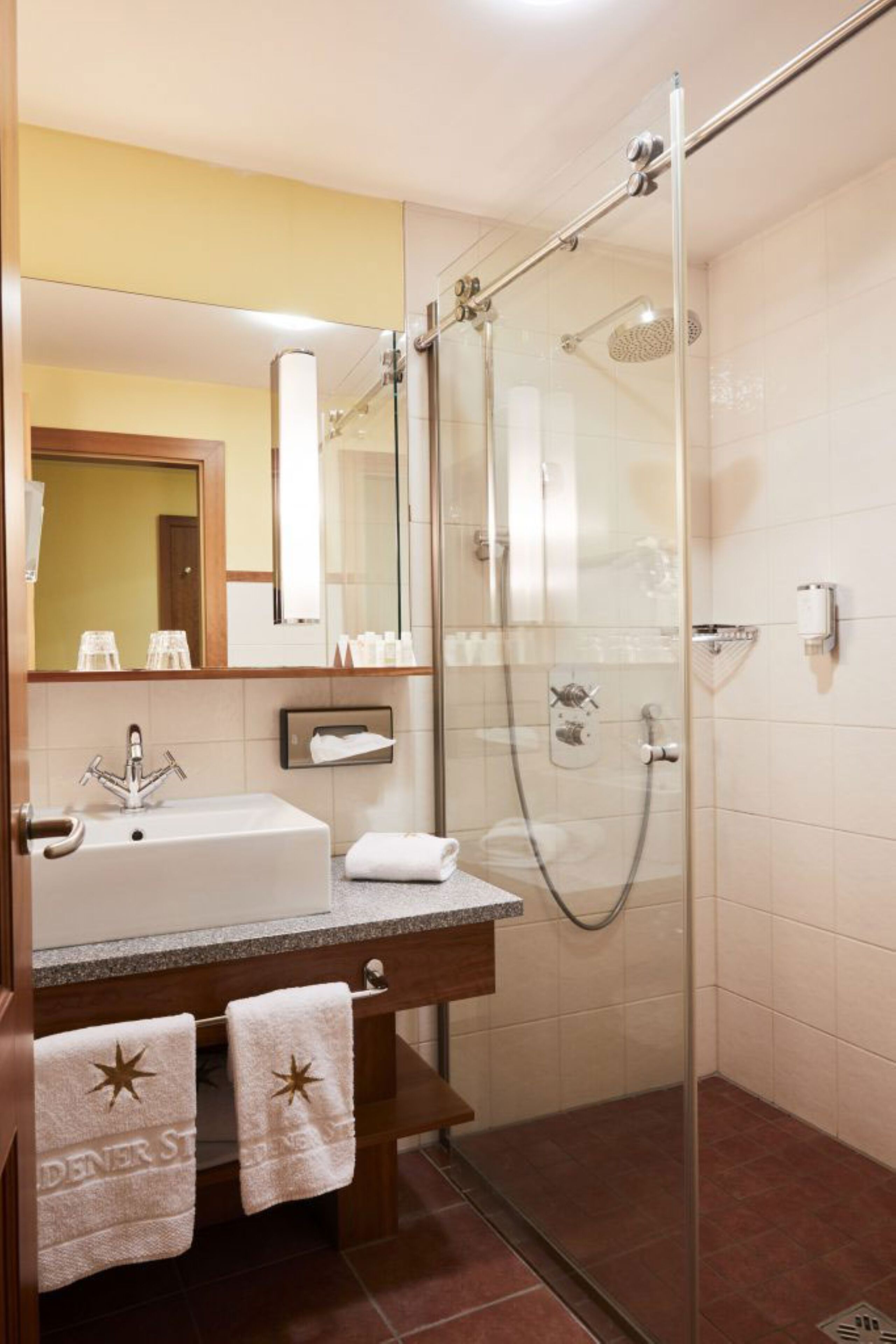 Un baño con ducha de vidrio, un lavabo con espejo y dos toallas colgadas en la pared.