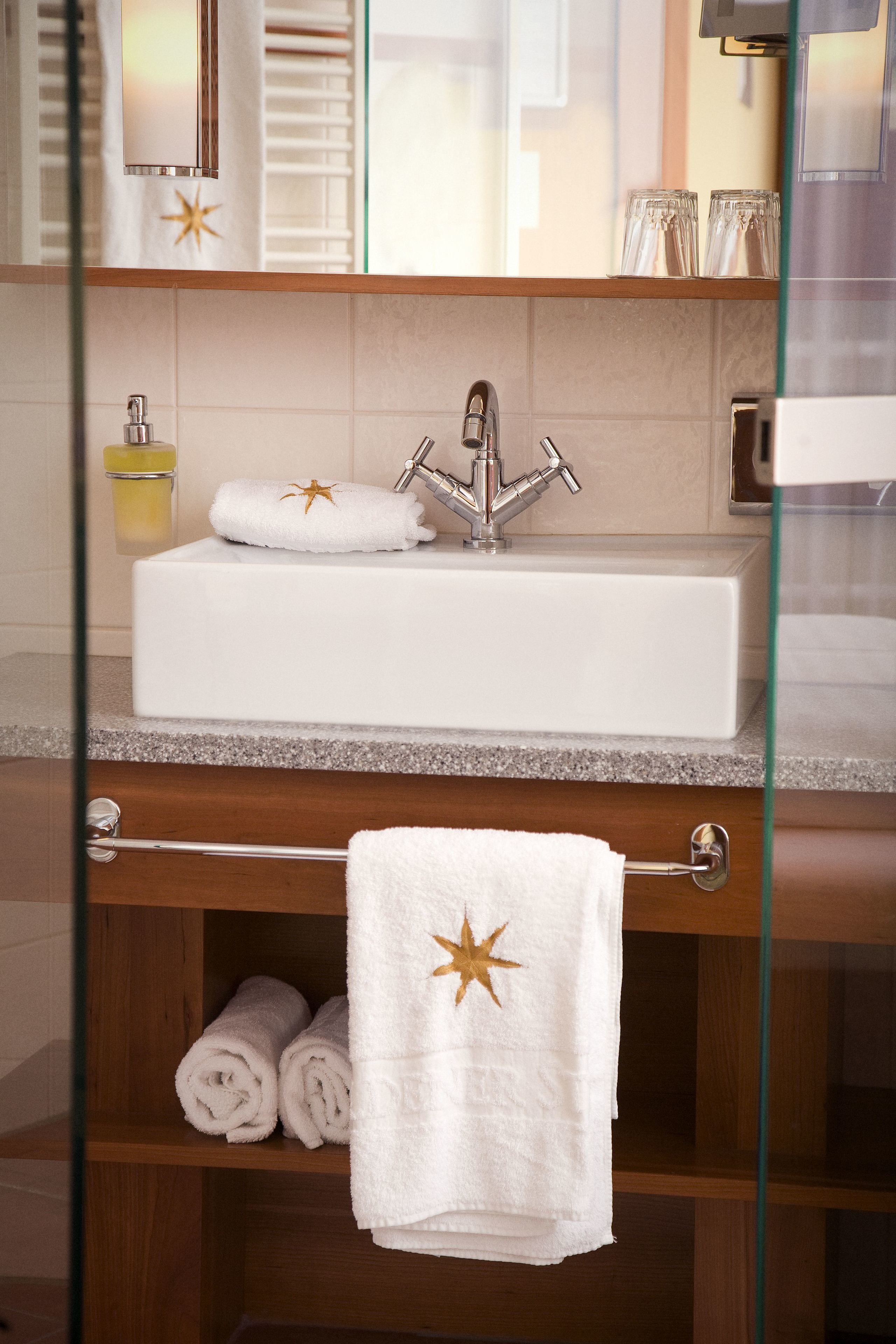 A bathroom with a white sink, a glass shower enclosure, and a wooden shelf with towels.