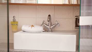 A bathroom with a white sink, a glass shower enclosure, and a wooden shelf with towels.