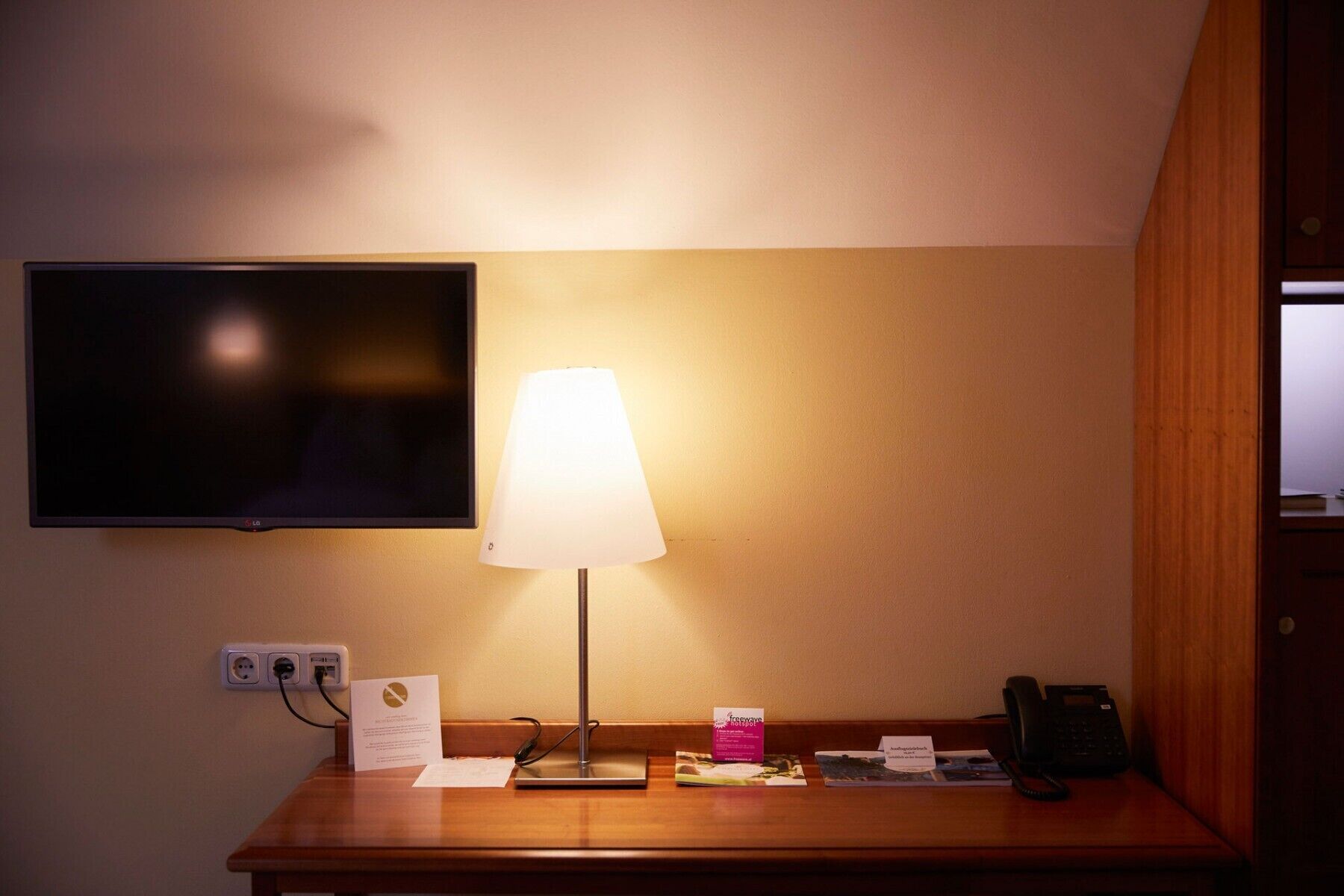 A hotel reception desk with a flat-screen TV, a table lamp, a phone, and some informational brochures.