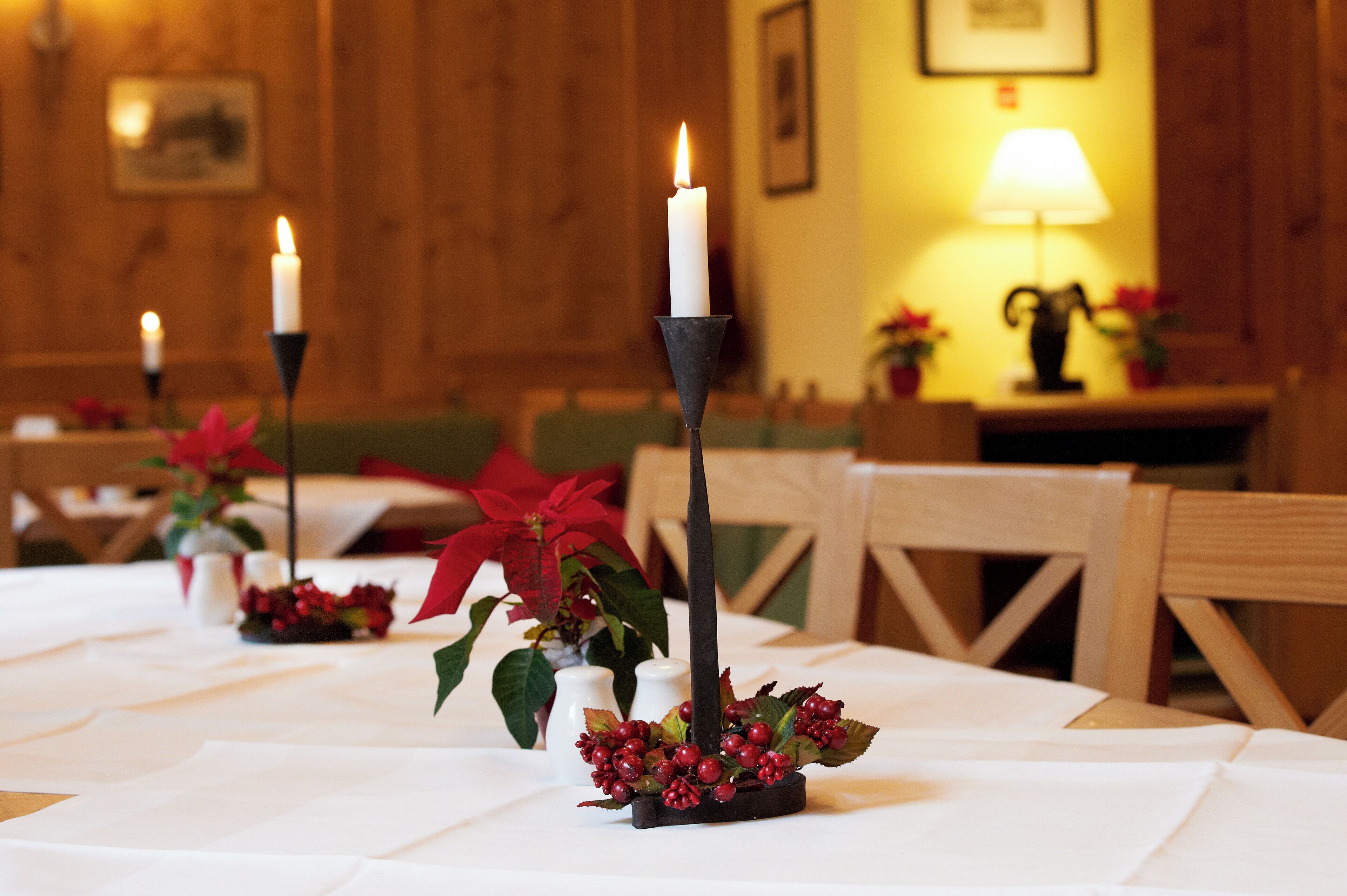 Un comedor con mesas dispuestas para el servicio, velas y plantas de poinsettia.