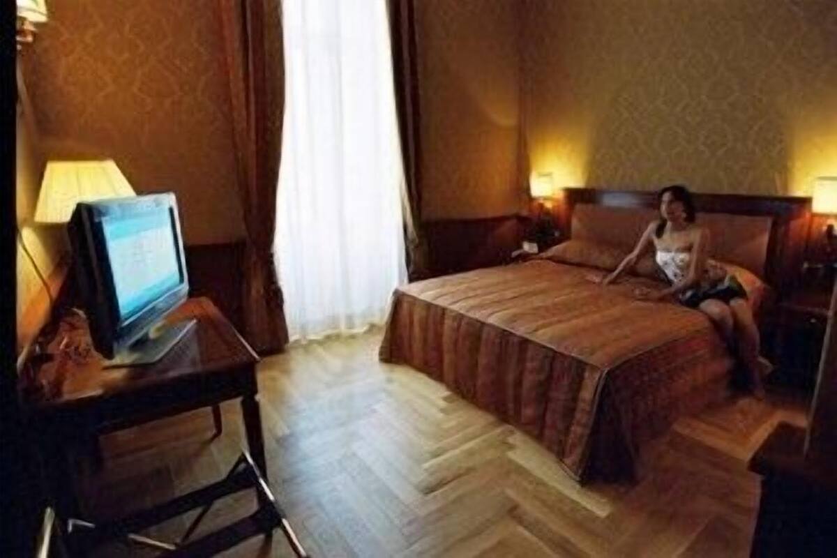 Une chambre d’hôtel avec un lit, un bureau avec un ordinateur et une fenêtre avec des rideaux.