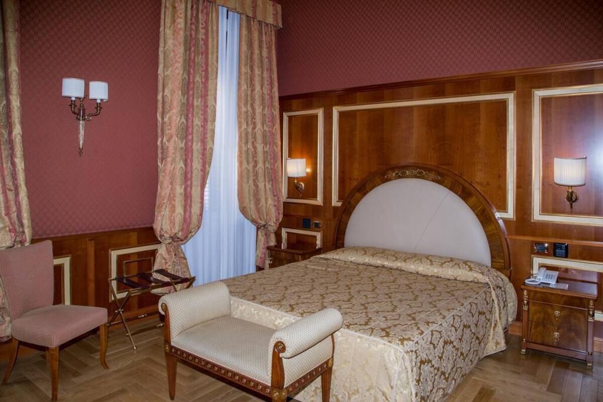 Une chambre d’hôtel avec un grand lit, deux tables de chevet, une chaise, un bureau et un miroir.