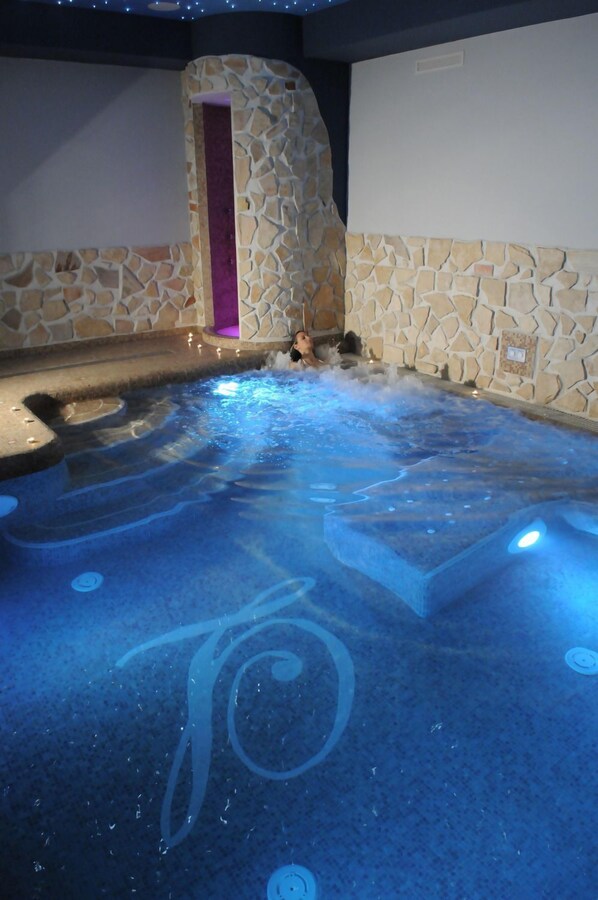 A hot tub with a stone wall backdrop and a purple-lit entrance. - Hotel Livingston Siracusa (Syracuse)