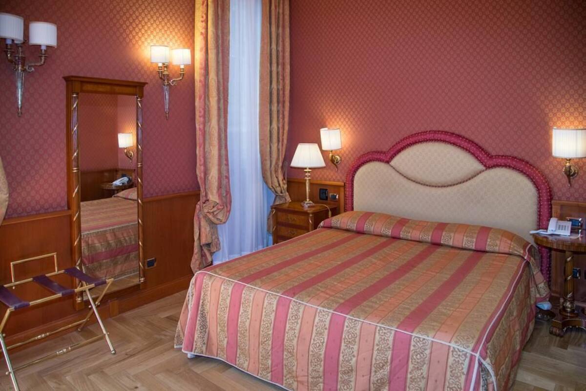 Une chambre d’hôtel avec un grand lit, une table de chevet en bois, un miroir et une chaise.