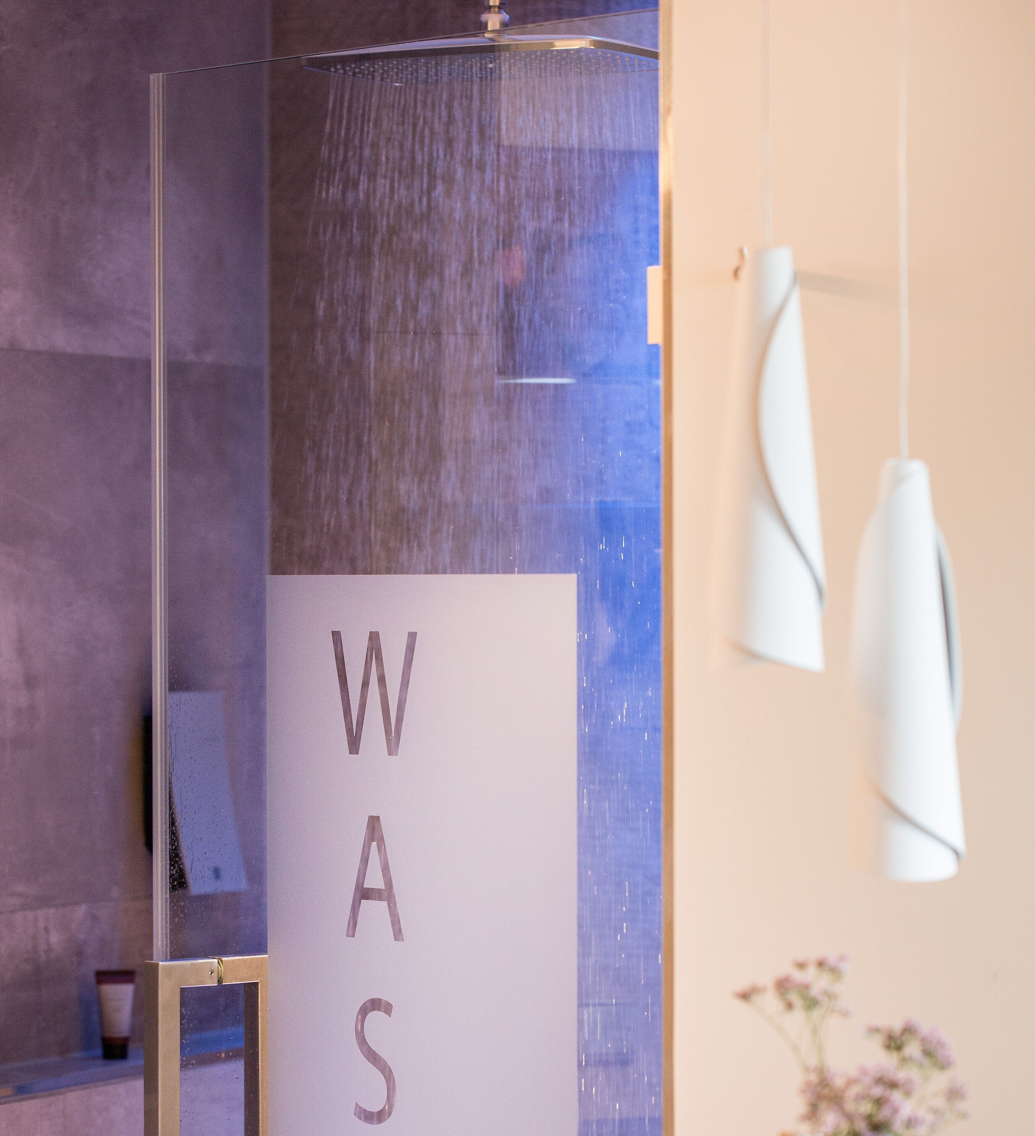 A bathroom with a glass partition, a towel rack, and a sign with the letters "WAS".