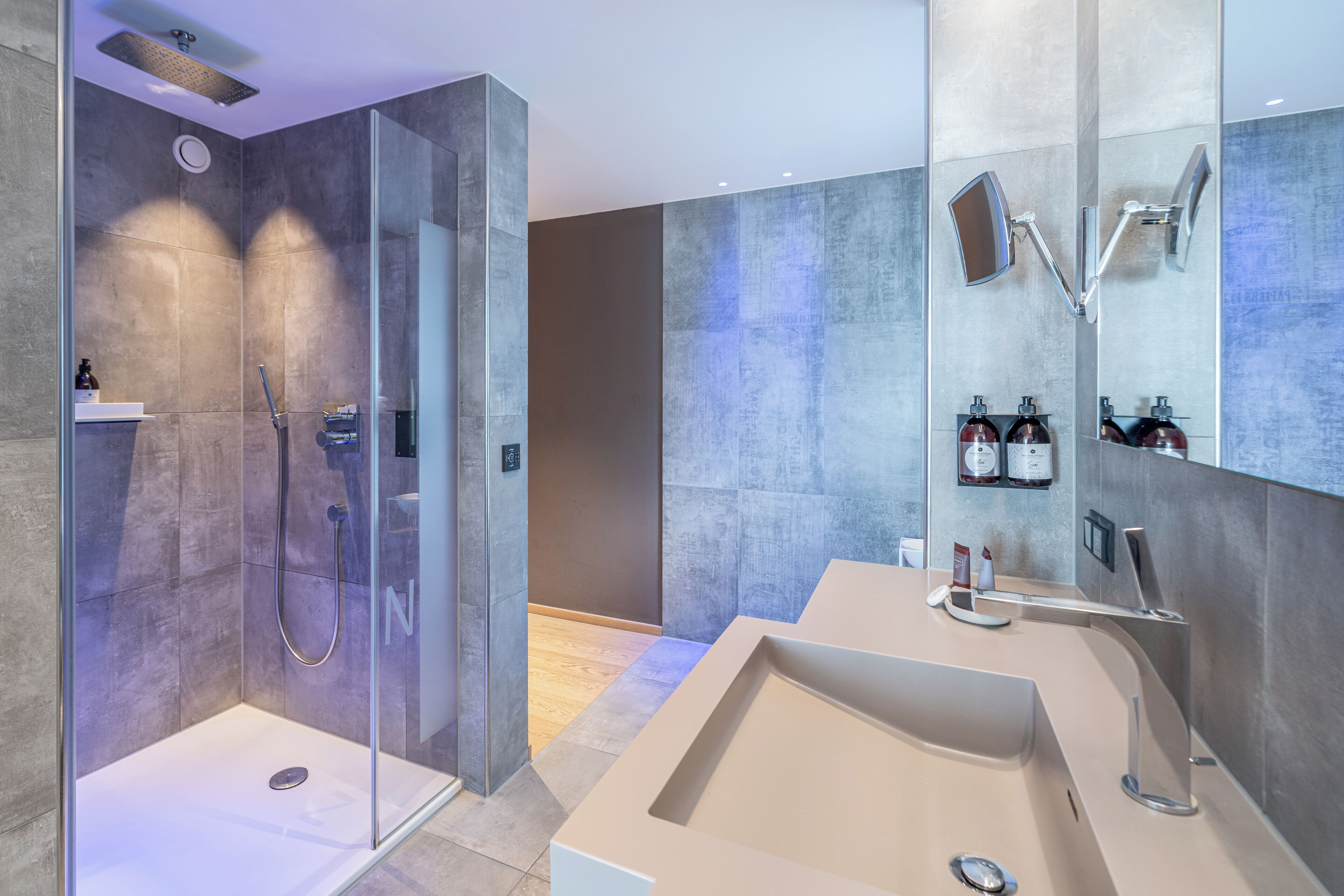 Une salle de bain moderne dotée d’une douche à parois de verre, d’un grand lavabo et d’un miroir avec éclairage intégré.