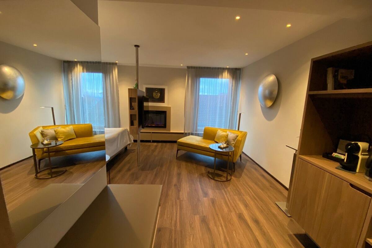 A modern hotel room with two yellow sofas, a flat-screen TV, a fireplace, and a wooden cabinet.