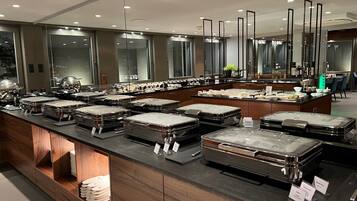 A buffet area with multiple serving stations, each with a covered food container. There are wooden cabinets below the buffet, and a large mirror above the counter.