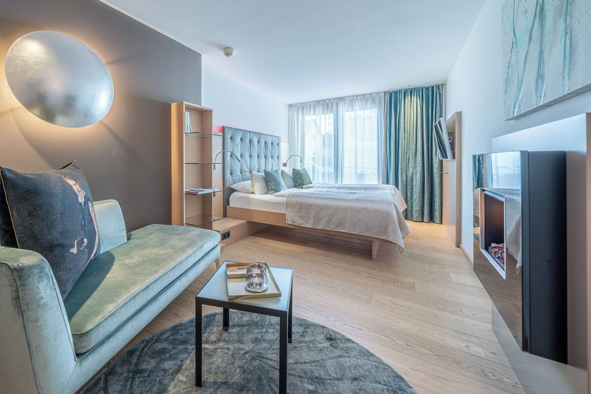 A modern hotel room with a bed, a sofa, a small table, and a TV.