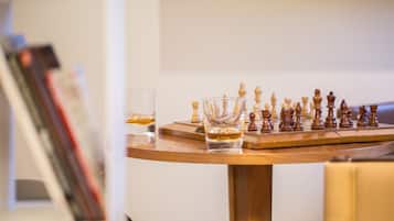 A chessboard on a wooden table with glasses and books in the background.