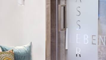 Un intérieur moderne avec une porte vitrée sur laquelle on peut lire « WASSERLEBEN » et un banc agrémenté de coussins.