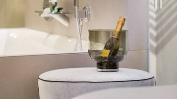 A modern bathroom with a bathtub, a glass bowl with a bottle of champagne, and a mirror reflecting a toothbrush and a wine glass.