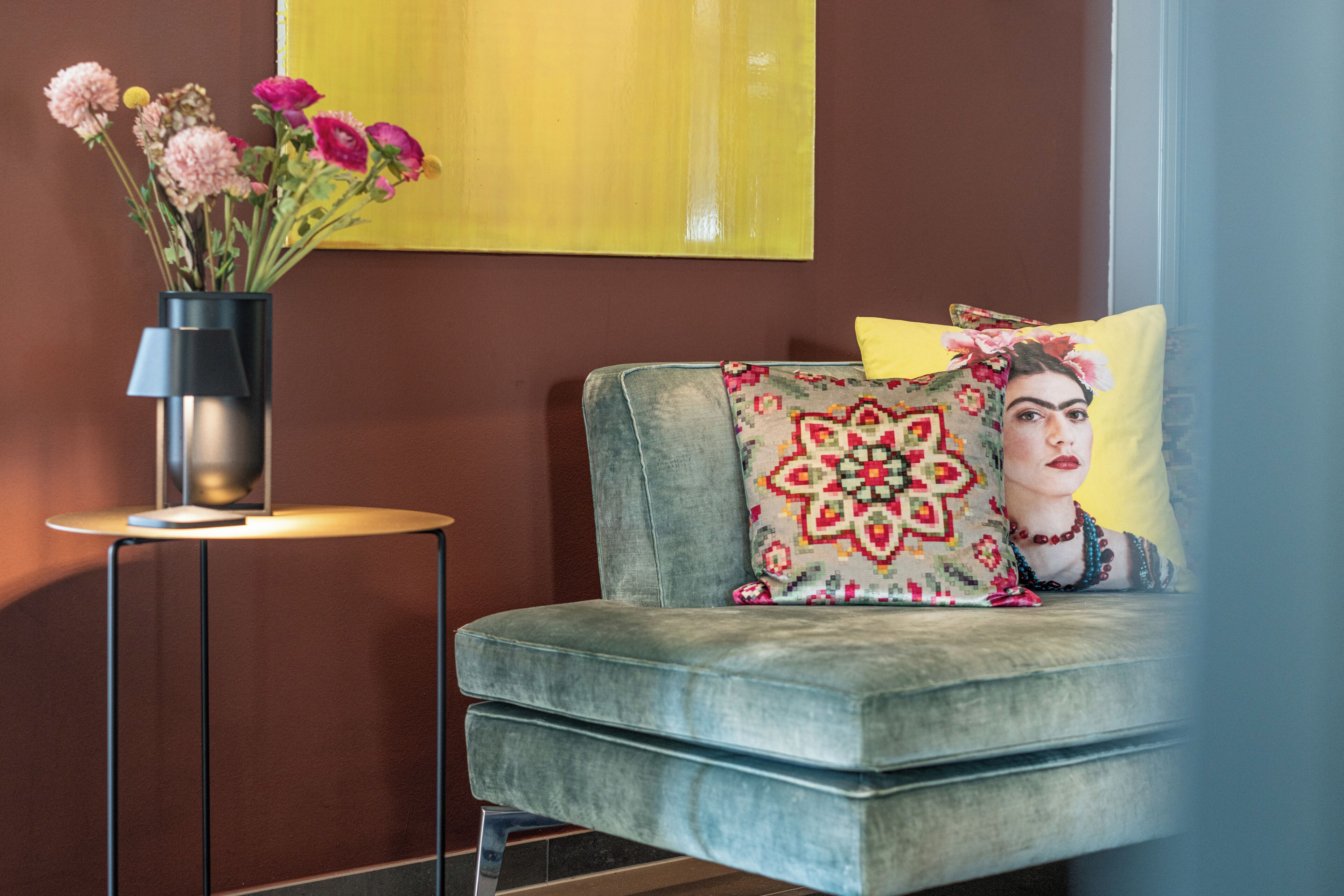 A modern living room with a grey sofa, a small round table with a black lamp, and a vibrant yellow wall.