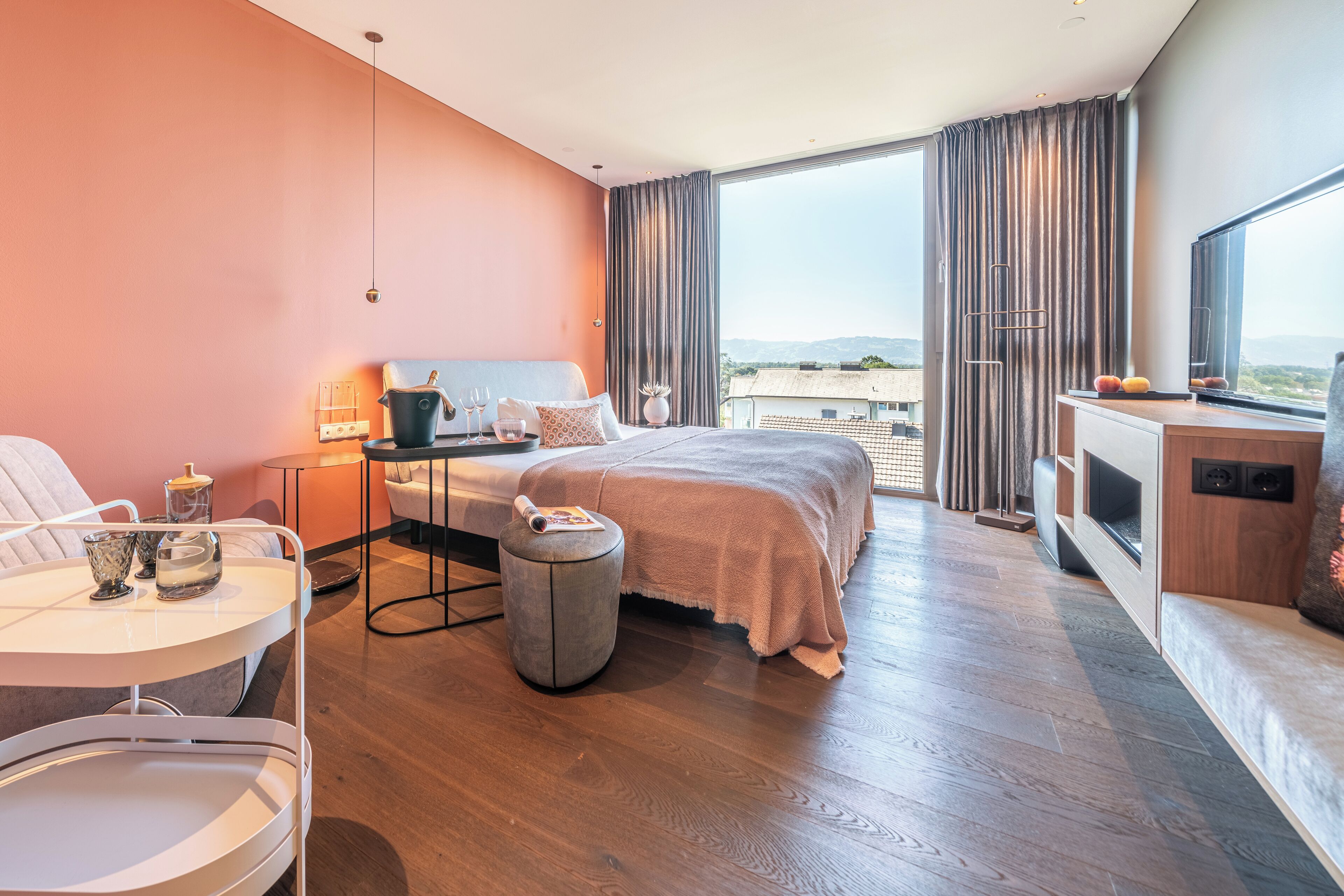 A modern hotel room with a large bed, a desk, a chair, and a view of the city.