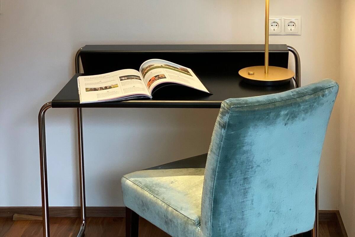 A modern room with a black desk, a blue chair, a framed abstract painting, and a floor lamp.